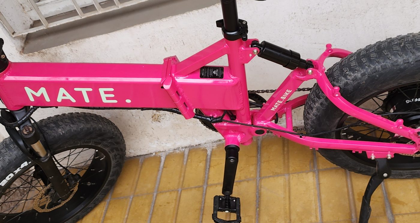 Bicicleta eléctrica fucsia de cuadro plegable con ruedas anchas, apoyada sobre su pata de apoyo.