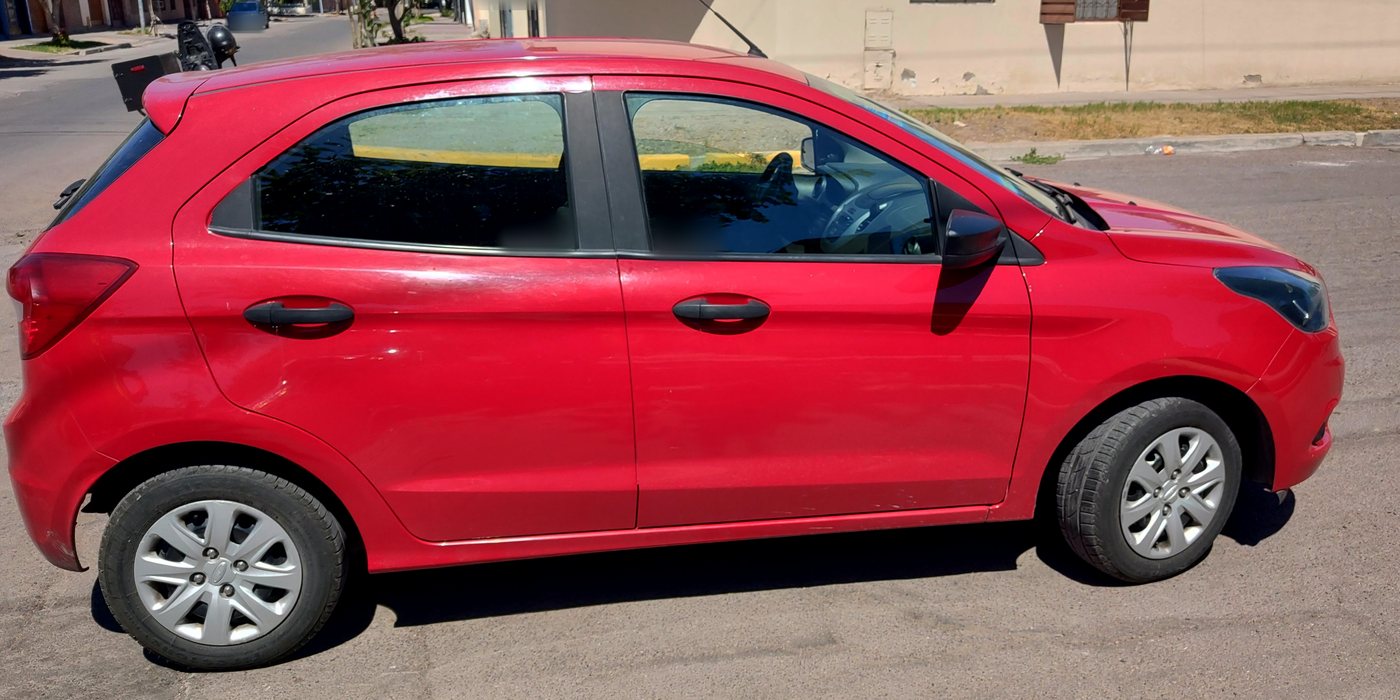 Ford Ka rojo estacionado en la calle, fotografiado de perfil. Las patentes están difuminadas.